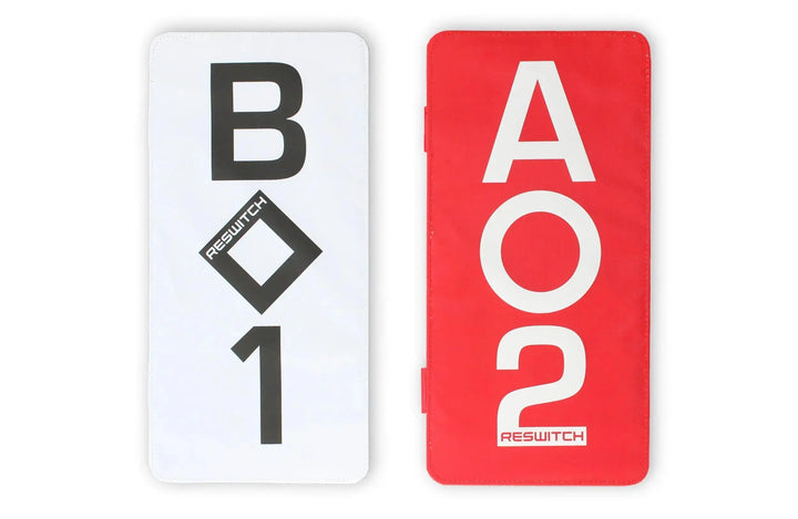 Das RESWITCH Pro-Coach Set von matchconcept UG enthält zwei rechteckige Karten - eine weiße mit fetter schwarzer "B 1" und einer Raute, eine rote mit fetter weißer "A 2". Beide verfügen über RESWITCH und sind praktisches Trainingszubehör Fußball.